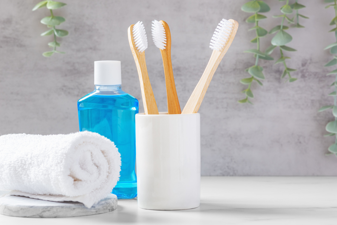 Bamboo toothbrushes in white cup with mouthwash and towel, dental health care background